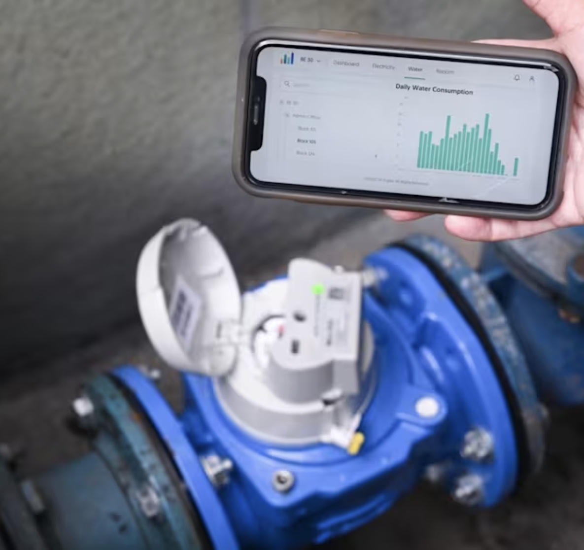 A smart water meter fitted to a water main, with a phone showing its daily consumption dashboard